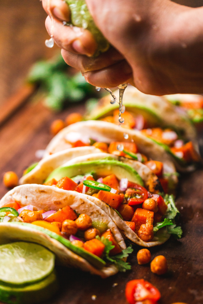 Close-up of shrimp tacos with spicy coleslaw, lime wedges, fresh cilantro, and avocado slices.