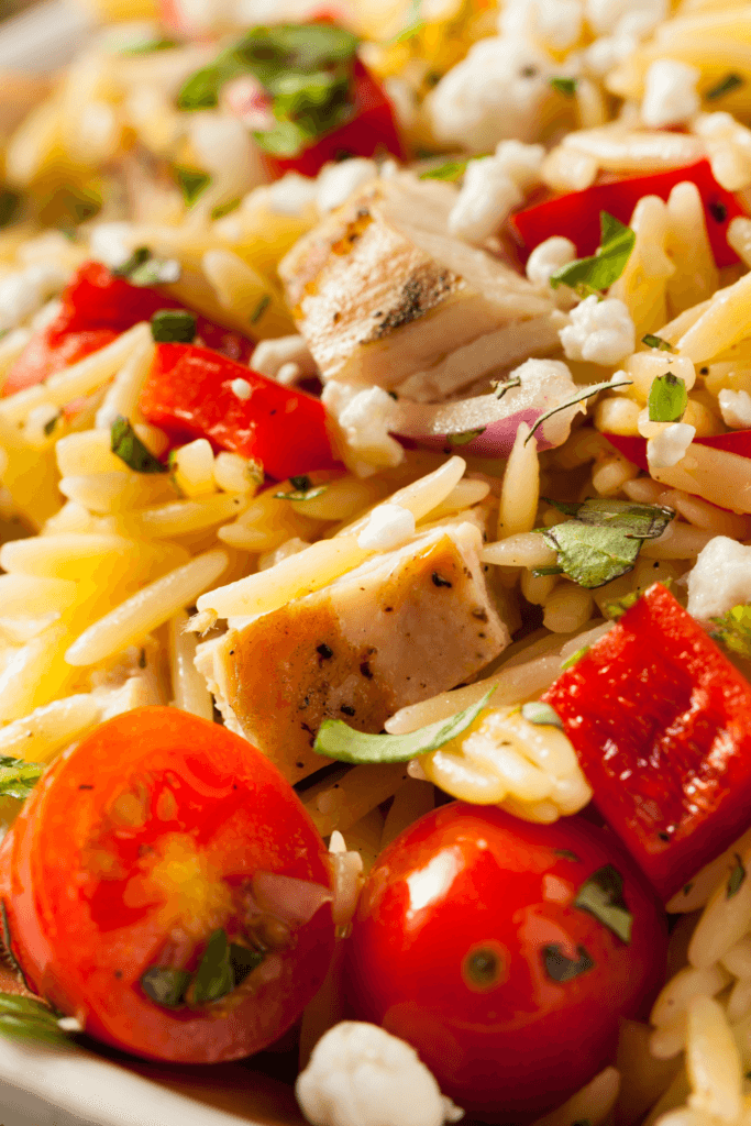 A close-up view of a Southwestern Chicken Orzo and Black Bean Skillet with grilled chicken, orzo pasta, cherry tomatoes, red bell peppers, black beans, fresh herbs, and crumbled cheese.