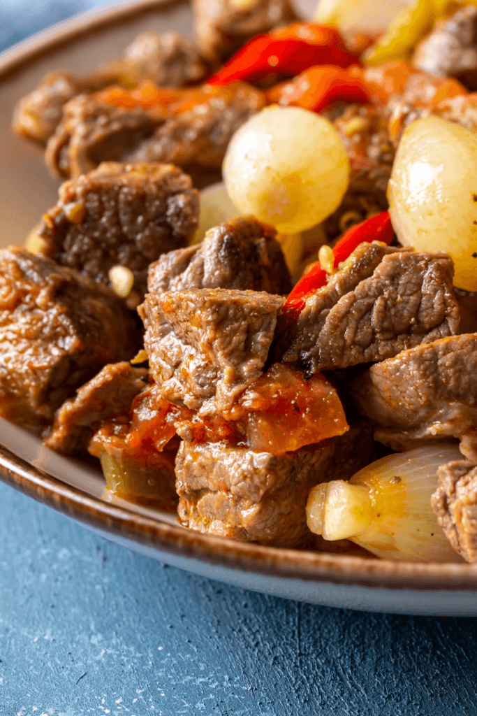 Close-up view of Carne Guisada, a traditional Mexican beef stew with chunks of beef, pearl onions, red bell peppers, and tomatoes.