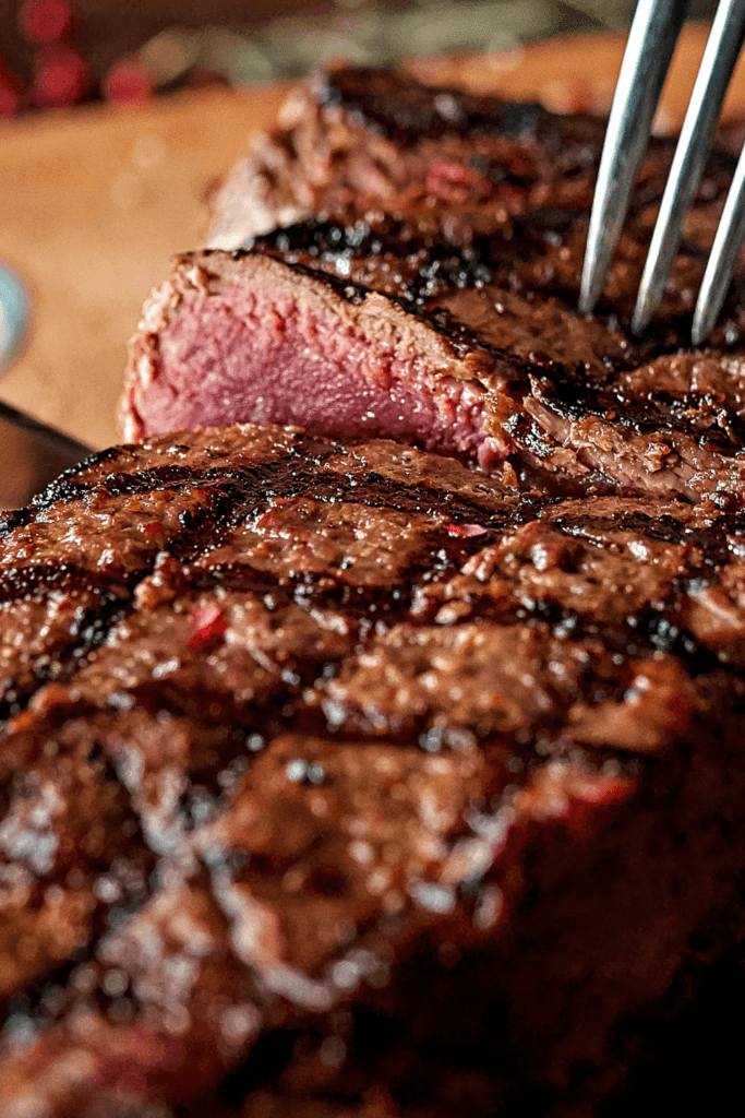 A close-up of a perfectly cooked steak with a seared, grilled exterior and a juicy, pink interior, with a fork inserted into the steak.