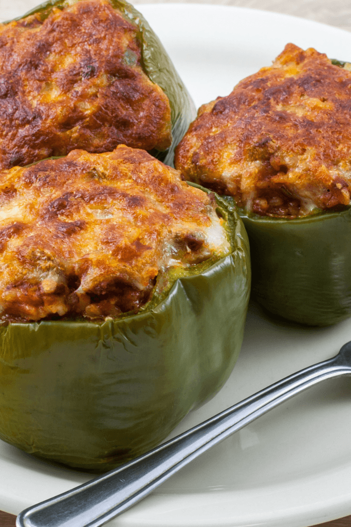 Three beef-stuffed poblano peppers on a white plate, filled with ground beef and cheese, and baked to a golden brown.