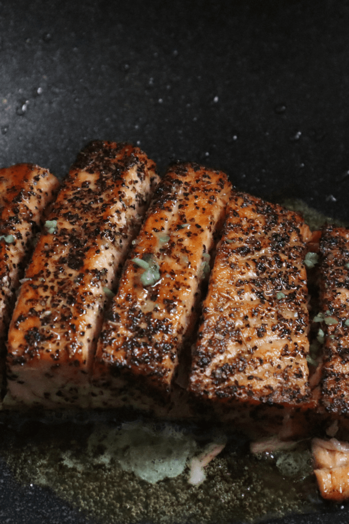Seasoned salmon fillets with a crispy, browned exterior, cooked in an air fryer, arranged in a row with melted butter or oil visible at the bottom.