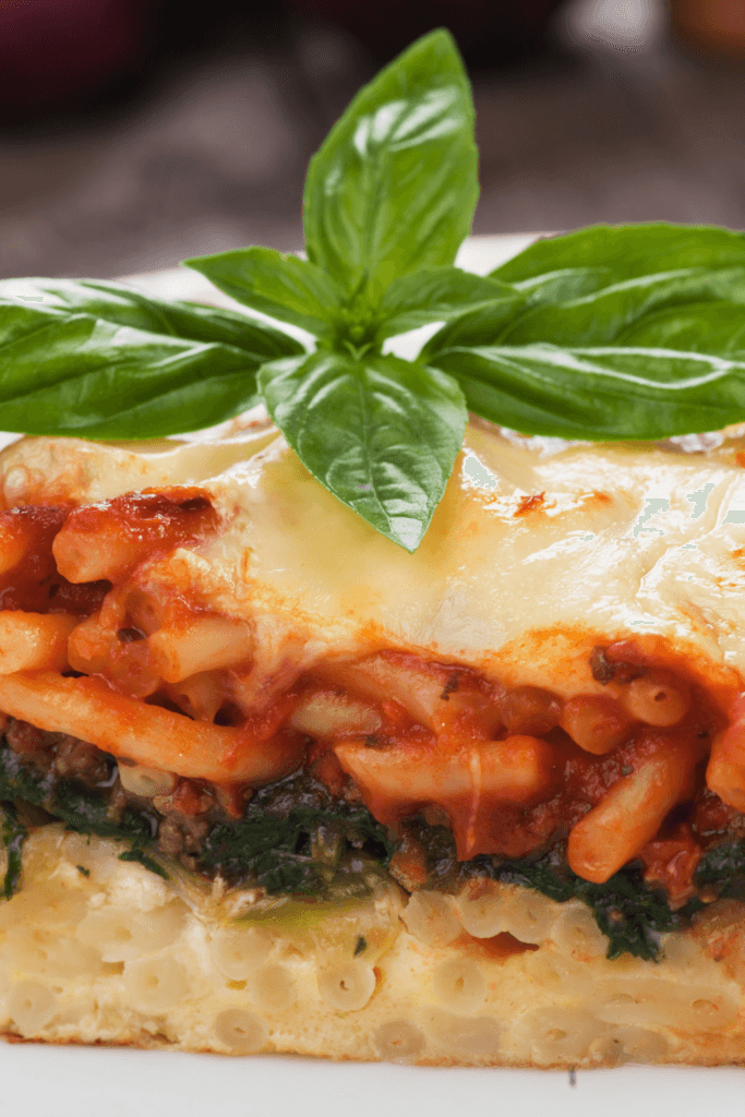 A close-up view of a slice of vegan pastitsio, featuring layers of pasta, tomato-based sauce, and creamy vegan bechamel, garnished with fresh basil leaves.