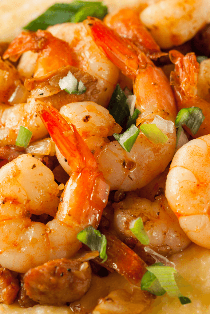 A close-up view of spicy shrimp cooked in a reddish-orange sauce, garnished with green onions and other vegetables.