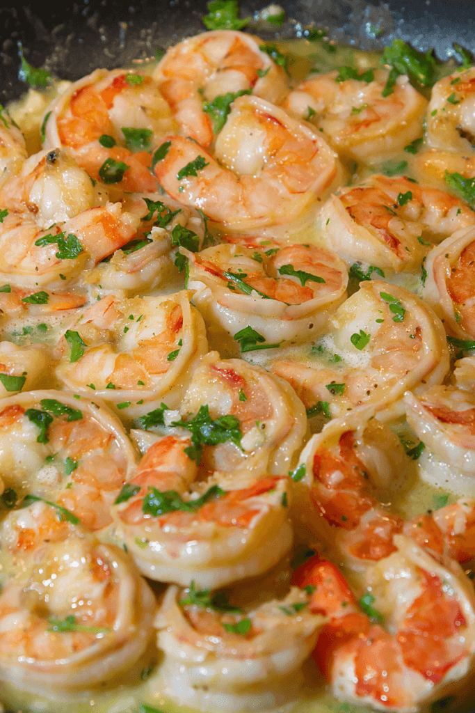 Cooked shrimp in a creamy garlic sauce, garnished with chopped parsley, presented on a white plate.