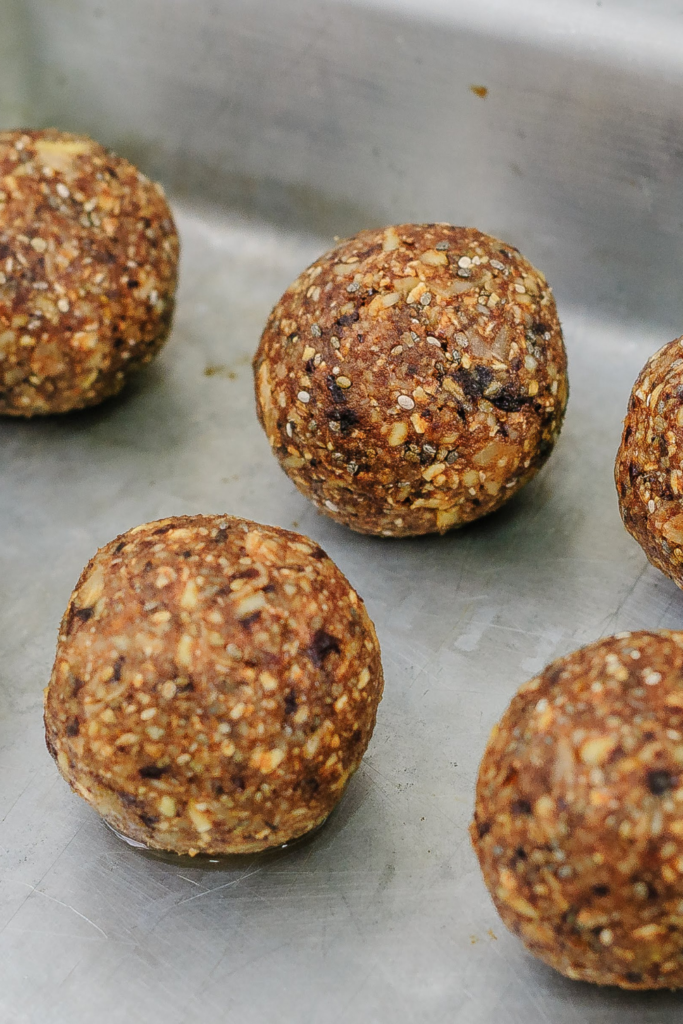 Five round, brown-colored protein balls made with oats and seeds, placed on a metal surface.