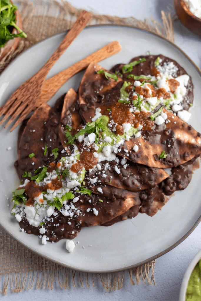 A plate of enfrijoladas with black bean sauce, crumbled cheese, cilantro, and red salsa.