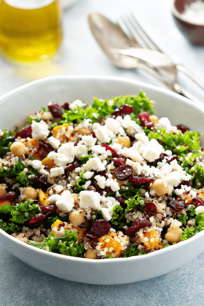 A bowl of Greek Vegan Chickpea Salad with chickpeas, quinoa, kale, dried cranberries, and crumbled vegan feta cheese.