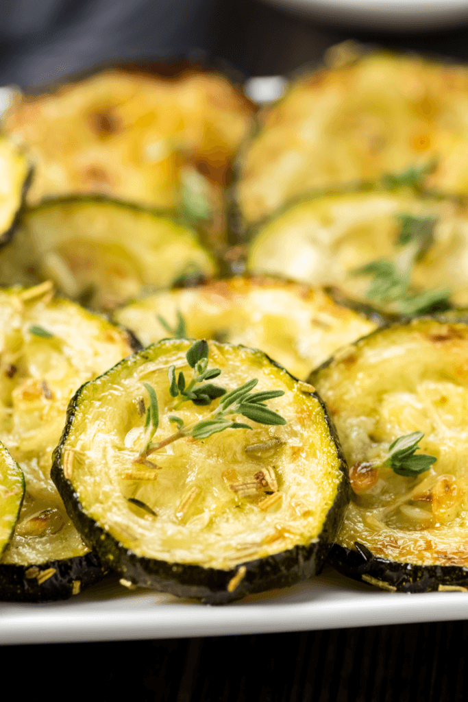 A close-up of a plate of air-fried zucchini slices, garnished with herbs and seasoned with spices, cooked to a golden-brown texture.