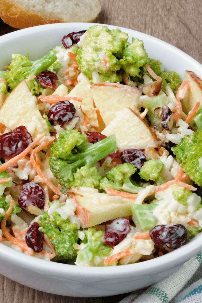 A bowl of Greek Yogurt Chicken Salad with pieces of chicken breast, broccoli florets, apple slices, shredded carrots, and dried cranberries, all tossed in a creamy dressing.