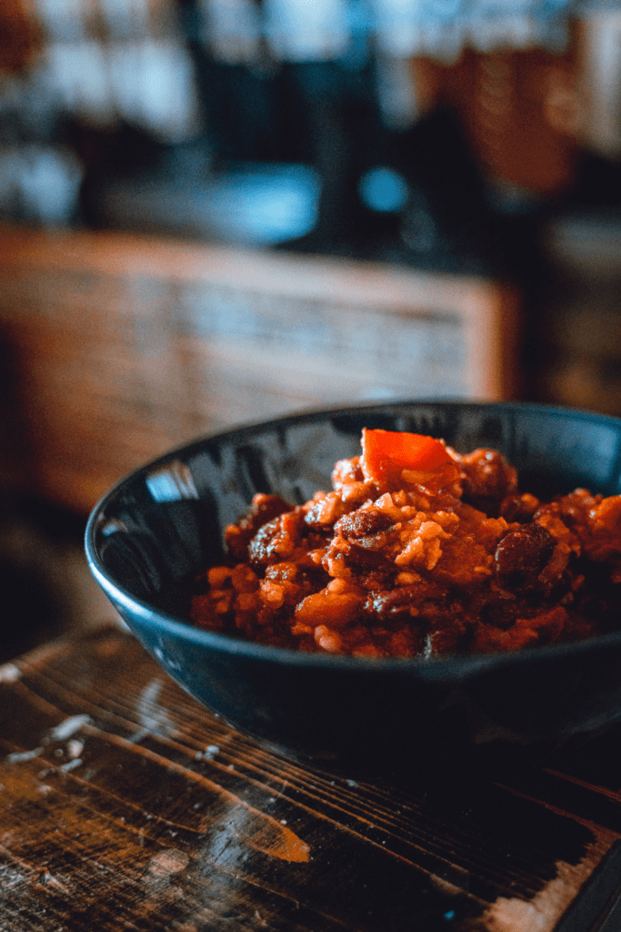 A close-up of a bowl filled with vegan chili sin carne, containing beans, rice, and vegetables in a rich, red sauce.