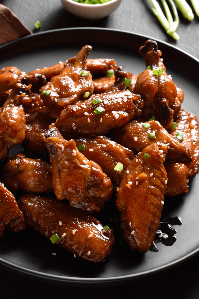 A plate of soy maple glazed chicken wings garnished with sesame seeds and chopped green onions, served with roasted sweet potatoes.