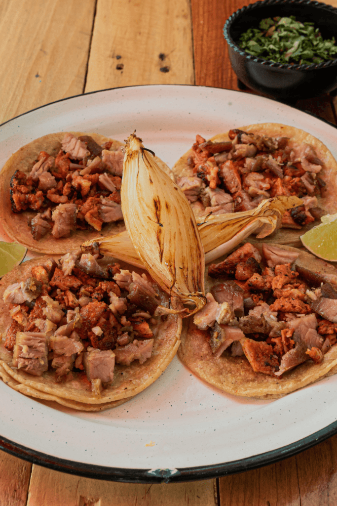 A plate of Carne en su Jugo, a traditional Mexican beef and bacon stew, garnished with fresh cilantro and lime wedges.