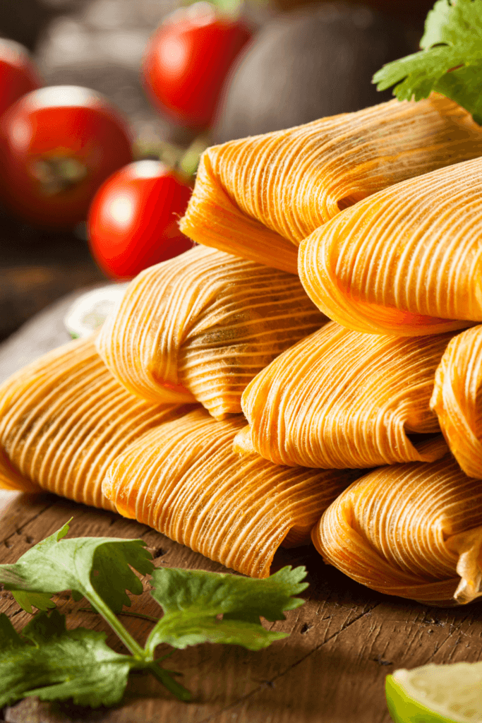 Close-up of pulled pork tamales wrapped in corn husks, garnished with fresh cilantro and lime wedges.