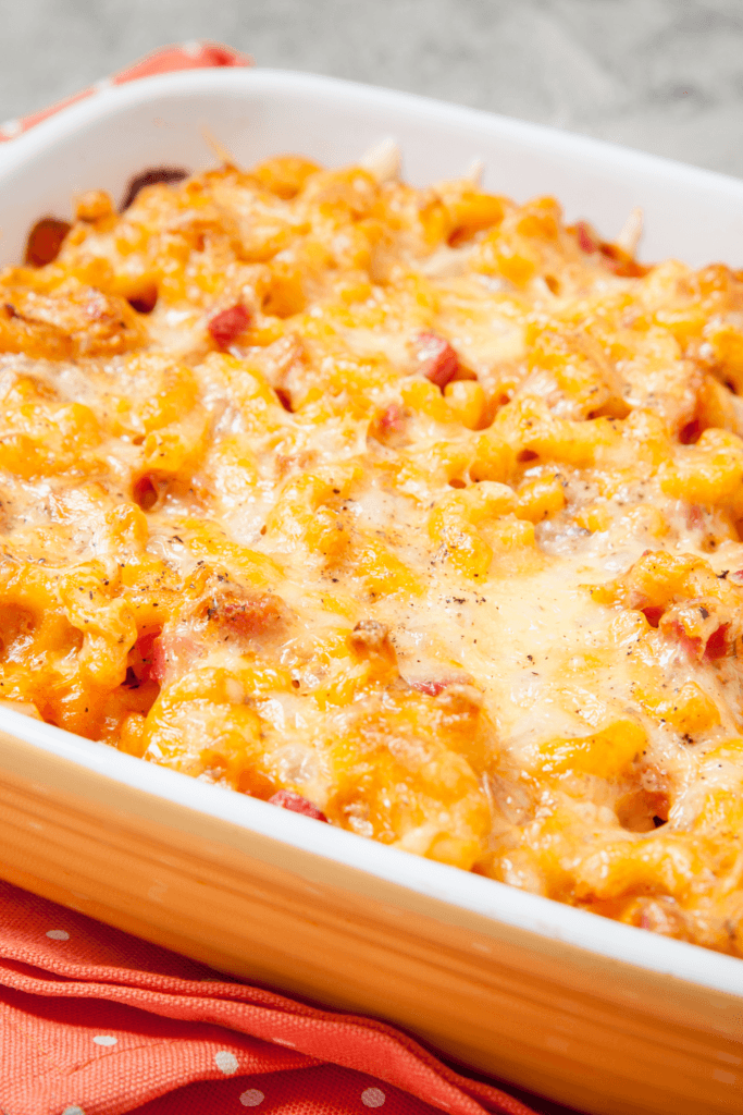 Close-up of baked mac and cheese in a rectangular baking dish, with macaroni pasta covered in a creamy, melted cheese sauce, featuring some browned and crispy edges.