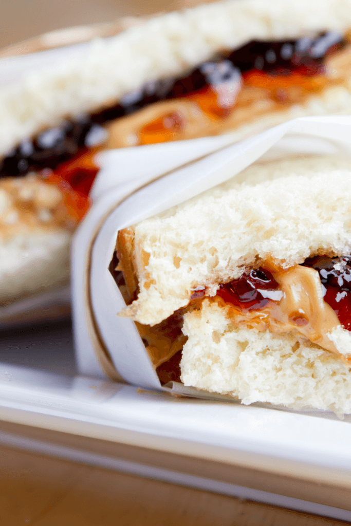 Close-up of a grilled peanut butter and jelly sandwich, cut in half and wrapped in white paper, with peanut butter and jelly oozing out from between the slices of toasted bread.