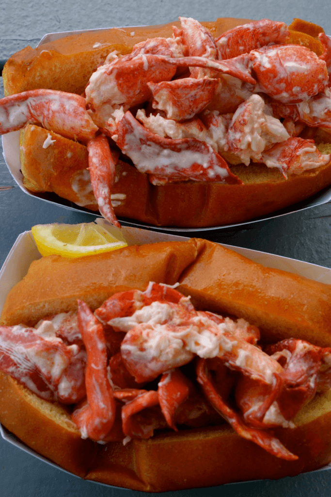 Two lobster rolls with creamy dressing in toasted split-top buns, one with a lemon wedge.