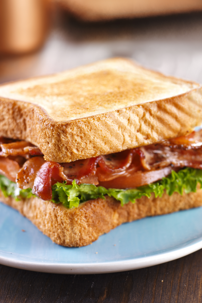 Close-up of a BLT sandwich with crispy bacon, fresh green lettuce, and tomato slices, served on a blue plate.