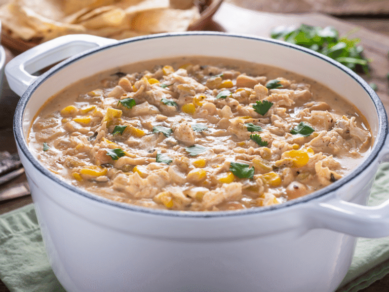 Bowl of creamy Easy Crockpot White Chicken Chili topped with cilantro, shredded cheese, and sliced jalapeños.